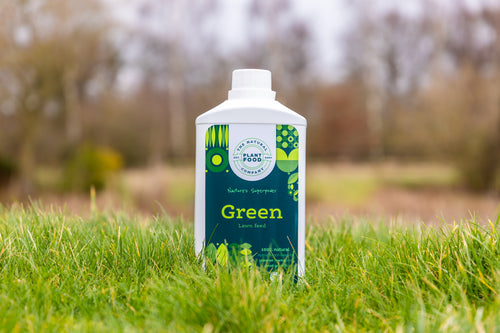 Green lawn feed 1L bottle standing in long grass, trees soft in the background