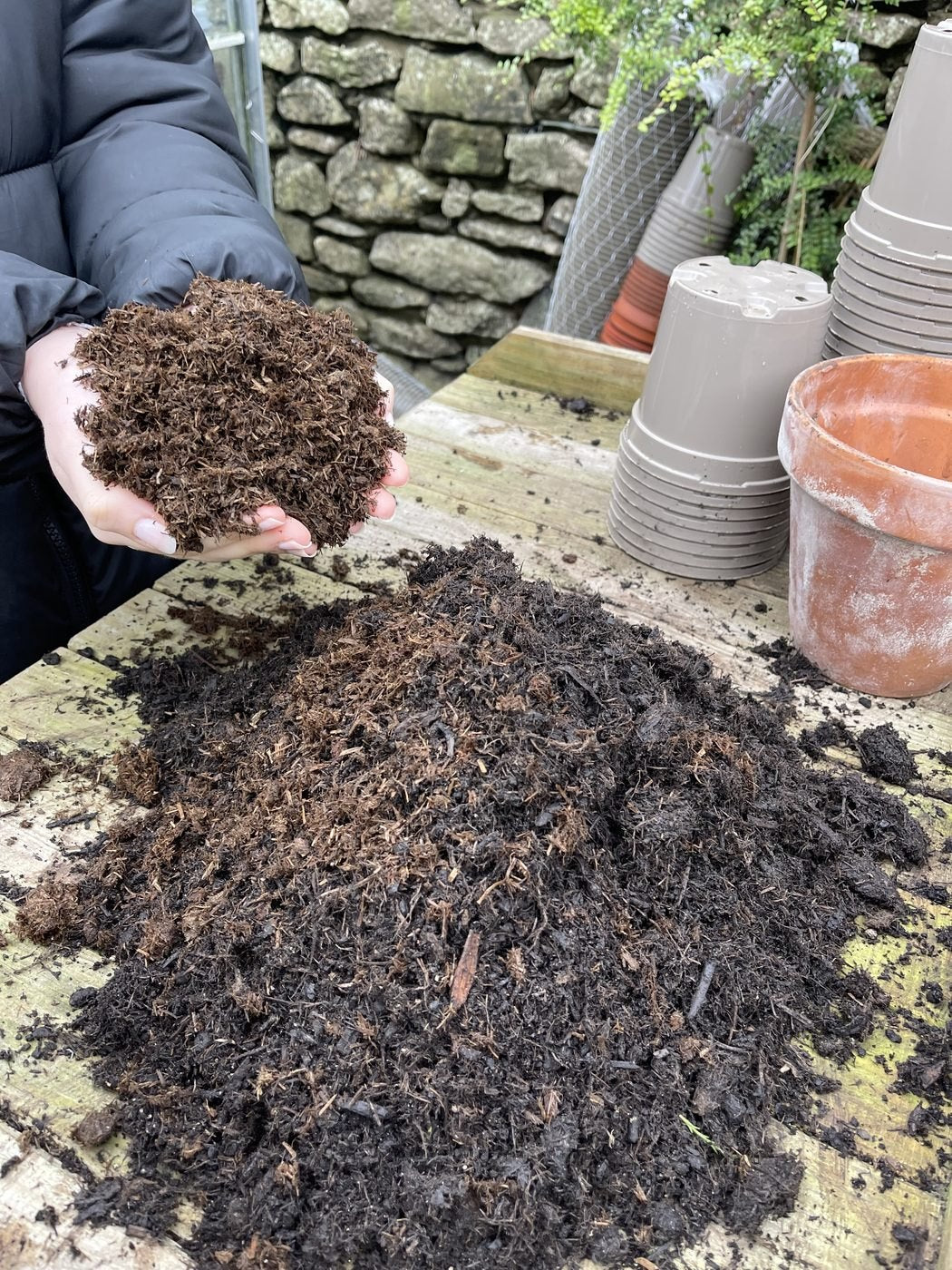 A large heap of dark compost on a potting bench with a handful held above it