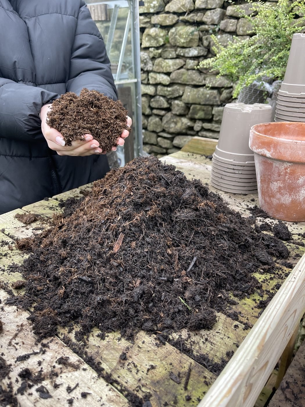 Hands holding a handful of dark, crumbly compost above a heap on a potting bench