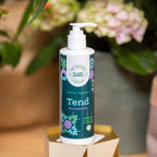 Tend houseplant food in a 250ml pump bottle on a small gold plinth, with pink hydrangea flowers and terracotta pots behind