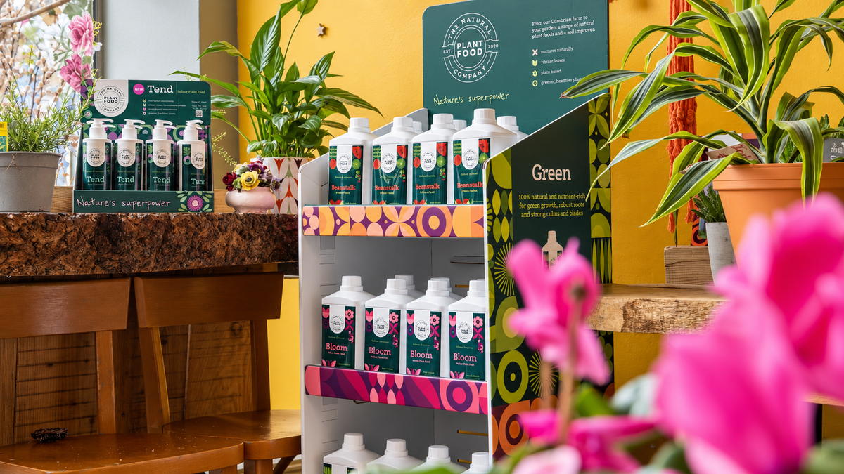 NPFC point-of-sale displays in a real shop: the Tend countertop display on the left and the freestanding range stand in the centre, among houseplants